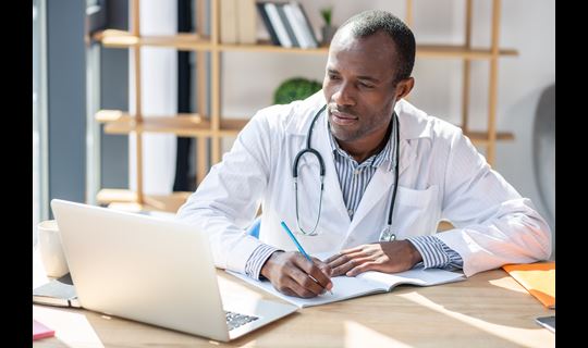 Doctor looks at laptop and takes notes